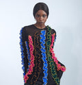 Person wearing a black outfit with colorful ruffled sleeves and patterned pants on a white background