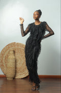 Woman in a black dress standing next to a large woven basket against a white wall.
