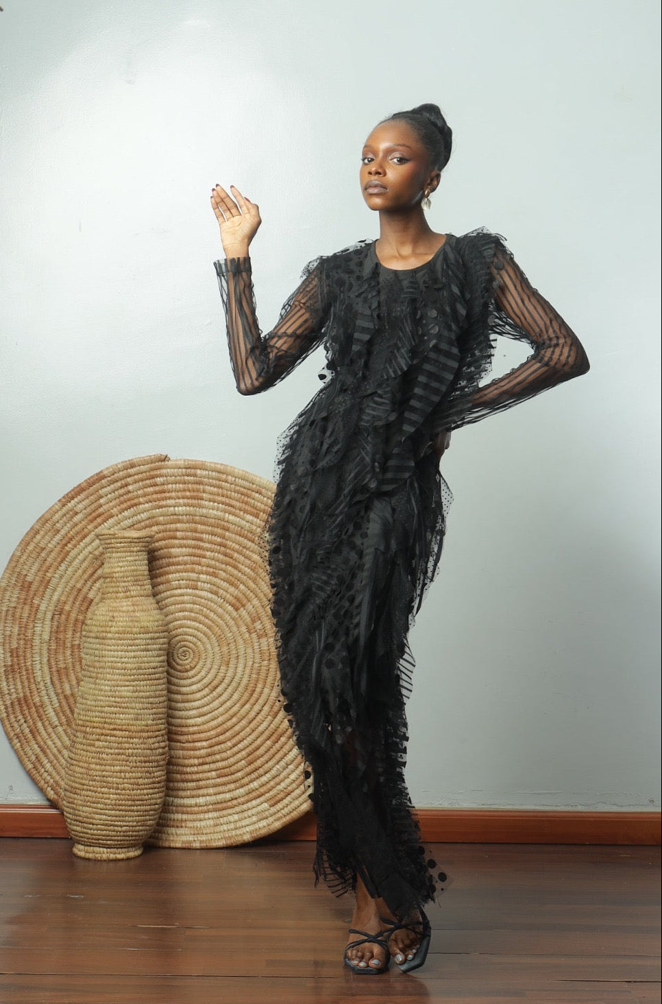Woman in a black dress standing next to a large woven basket against a white wall.